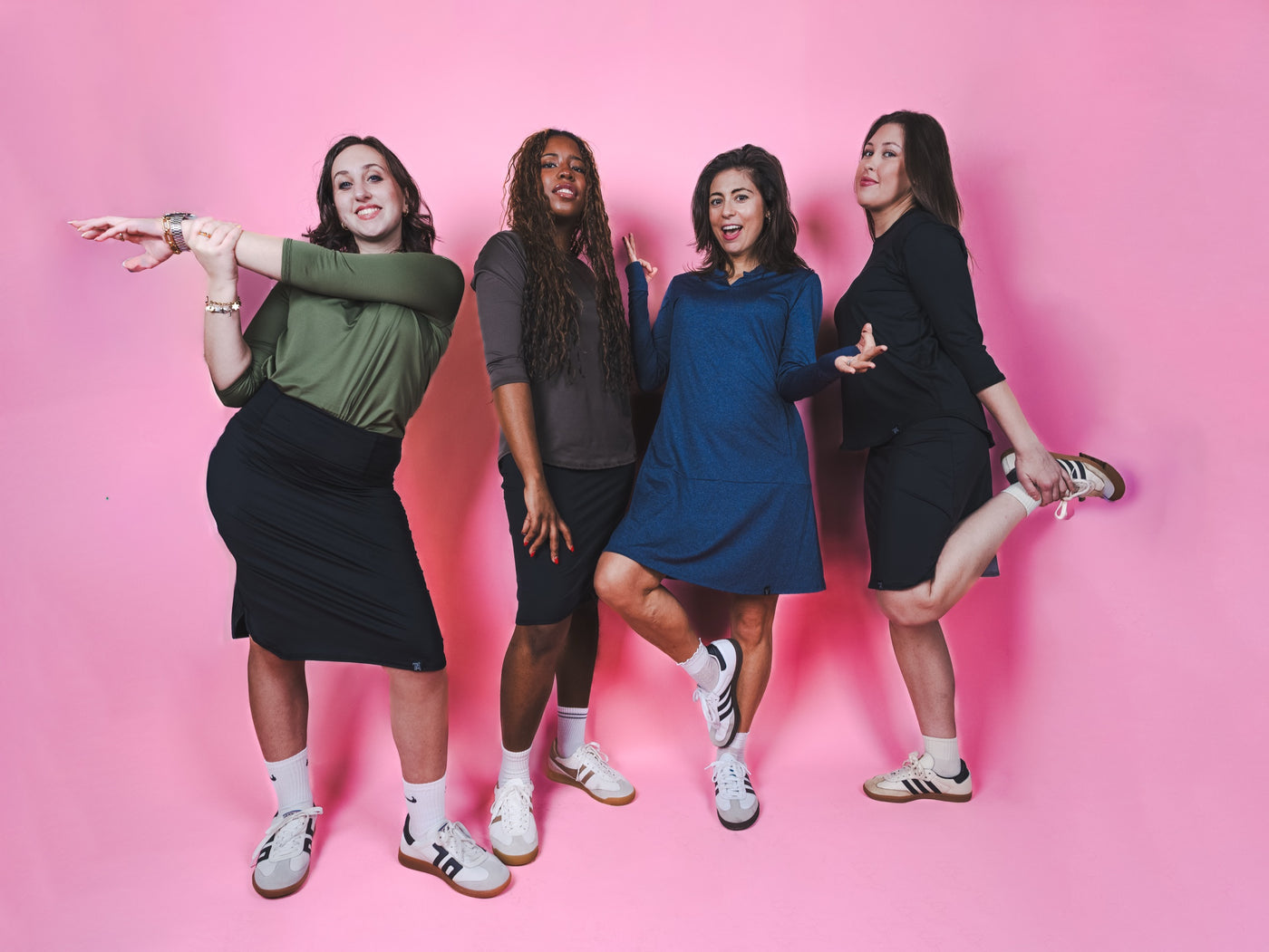 Four women in modest activewear skirts and tops against a pink studio backdrop